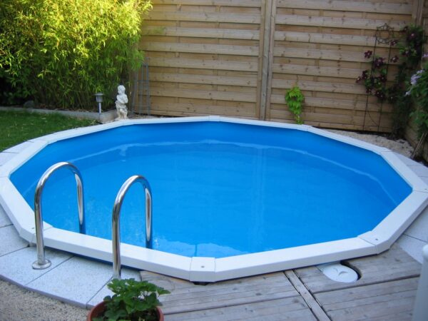 Cranpool-Riva ist der Pool für jeden Garten. Das Bild zeigt einen runden Cranpool Riva. Im Hintergrund ist ein Sichtschutz aus Holzelementen. Am Poolrand des versenkten Beckens Riva sind helle Pflastersteine verlegt.