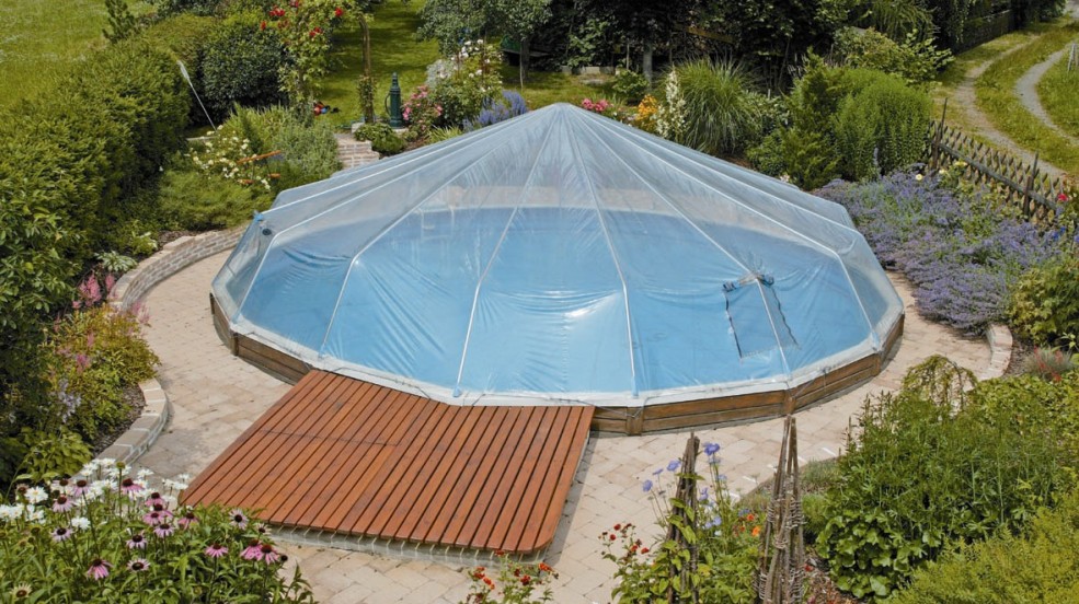 Cranpool Sonnendom sorgt für höhere Wassertemperaturen. Das Bild zeigt ein rundes Schwimmbecken Royal mit einem Sonnendom. Das Schwimmbecken befindet sich in einem schön angelegten Garten mit vielen verschiedenen Blumen und Sträuchern.