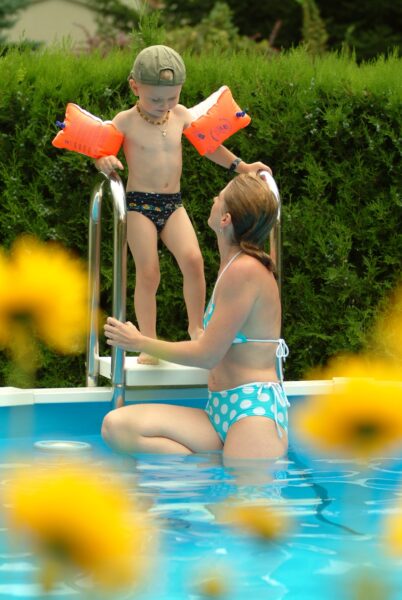 Cranpool Riva ist der Pool für jeden Garten. Das Bild zeigt einen kleinen Jungen auf der Einstiegstreppe stehend. Davor ist eine Frau an der Treppe angelehnt.