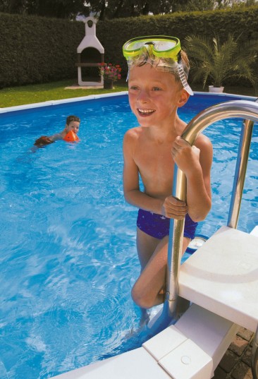 Stahlwand-Swimmingpool Royal ist die stabilste Konstruktion für runde und ovale Becken am Markt. Das Bild zeigt einen kleinen Jungen der auf der Eistiegstreppe steht und eine Taucherbrille am Kopf hat. Im Hintergrund schwimmt ein kleiner Junge im ovalen Becken Royal. Einen Hecke bildet den Sichtschutz zum Schwimmbecken. Vor der Hecke steht ein Griller.