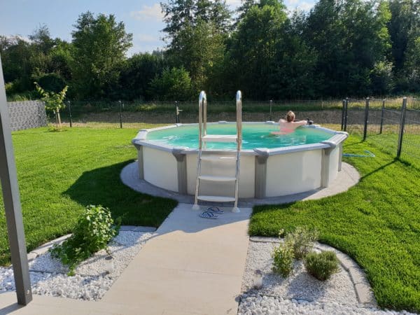 Frau badet im Rimini Rundpool, teilversenktes Aufstellbecken, Stahlwandbecken mit kristallklarem Wasser, Schwimmbad, Rimini Aktionsangebot, Gartenpool, Badepool im Garten; Poolbecken; Cranpool, Schwimmbecken mit Poolleiter, Swimmingpool mit Edelstahlleiter, Pool in schöner Gartenlandschaft