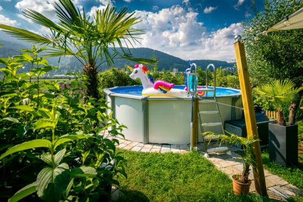 Aufstellbecken von Cranpool, in einem kleinen Garten mit palmen und vielen anderen Pflanzen. In dem kleinen Pool schimmt ein aufgeblasenes Wasserspielzeug