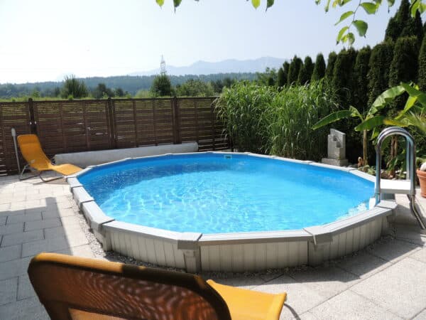Das ovale Stahlwandschwimmbecken von Cranpool ist ein teilweise eingegrabenes Pool, welches eine weiße Schwimmbadverkleidung hat. Auch gibt es eine Leiter mit weißen Sprossen in das Pool hinein.