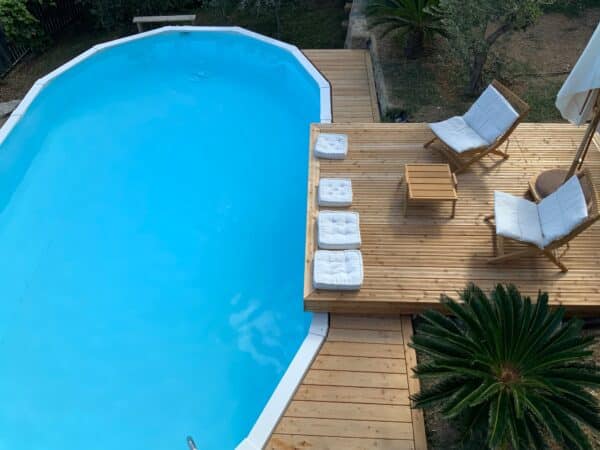 ovales Schwimmbecken von Cranpool mit Holzsteg mit Liegen und Polstern Sonnenschirm und einem Tisch