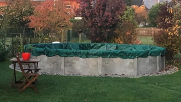 ovalbecken von Cranpool mit grauer Verkleiung und einer grünen Winterabdeckplane in einem Garten