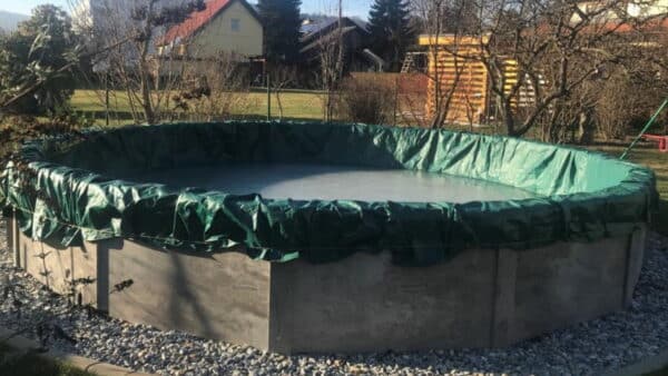 ovalbecken von Cranpool mit grauer Verkleiung und einer grünen Winterabdeckplane in einem Garten