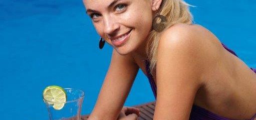 Junge blonde Frau liegt am Pool und trinkt einen Cocktail