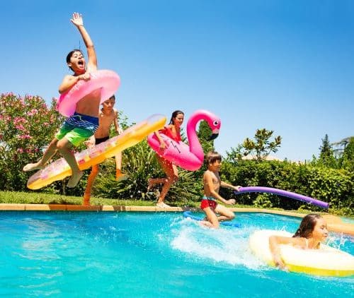 Kinder am Schwimmbecken und beim ins Wasser springen mit diversen Aufblasbaren Spielsachen