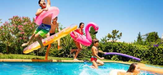 Kinder am Schwimmbecken und beim ins Wasser springen mit diversen Aufblasbaren Spielsachen