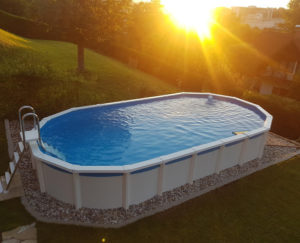 ein ovales Pool bei Sonnenuntergang. Das Schwimmbad ist von einem Beet aus kieselsteinen umgeben. Das Pool ist freistehend, oval und von Cranpool
