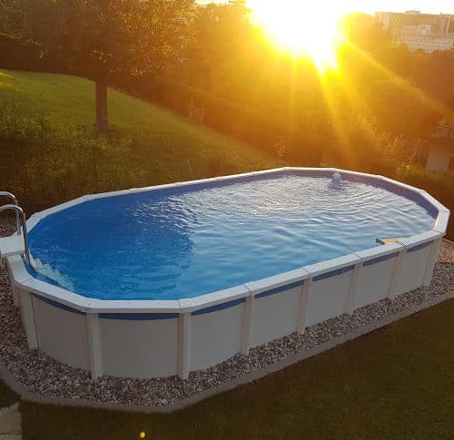 ein ovales Pool bei Sonnenuntergang. Das Schwimmbad ist von einem Beet aus kieselsteinen umgeben. Das Pool ist freistehend, oval und von Cranpool