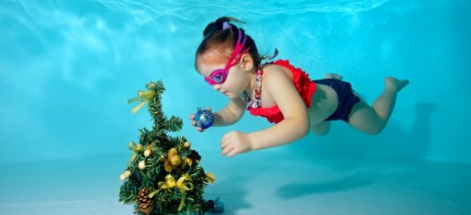 kleines Mädchen das einen Weihnachtsbaum Unterwasser in einem Schwimmbad dekoriert Child underwater in the pool decorates the Christmas tree with Christmas toys. Portrait. Shooting under water. Horizontal orientation