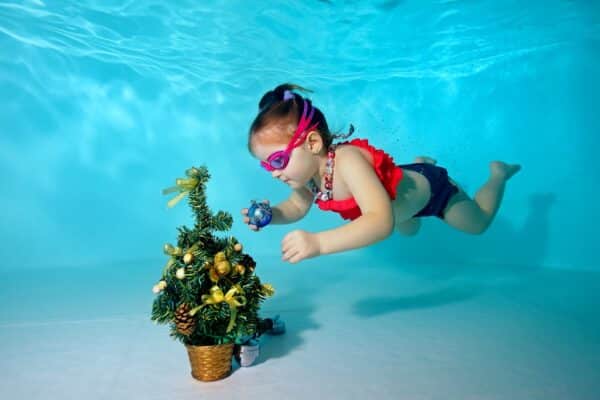 kleines Mädchen das einen Weihnachtsbaum Unterwasser in einem Schwimmbad dekoriert Child underwater in the pool decorates the Christmas tree with Christmas toys. Portrait. Shooting under water. Horizontal orientation