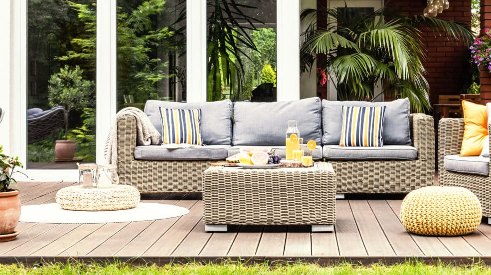 A relaxing spot for a warm, summer day - a stylish, wooden terrace with wicker garden furniture, cushions, plants and flowers