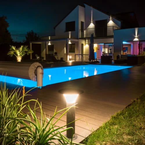 rechtckiger Pool mit offener Abdeckung in der nacht. Der Pool ist beleuchtet und hat einen Holzsteg runtherum.