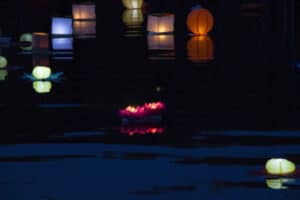 unbeleuchteter Pool bei Nacht mit diversen schwimmenden lampen, unteranderem seerosen und Lampions