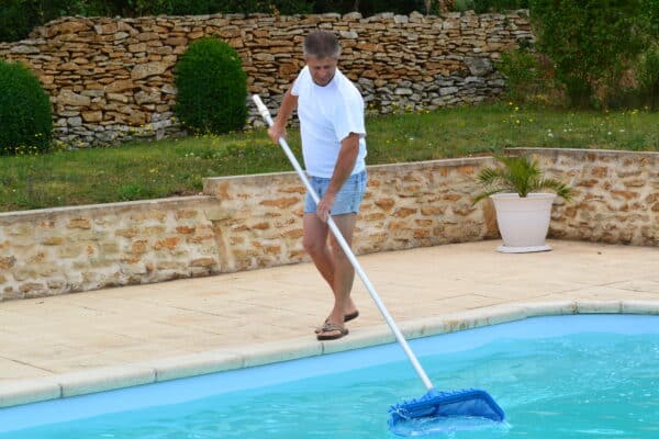 stolzer Cranpool Poolbesitzer beim reinigen seines rechteckigen Beckens mit einem kescher