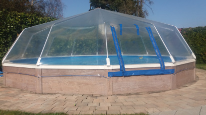 Ein rundes Schwimmbad mit einem Sonnendom und einer Holzverkleidung von Cranpool