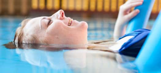 junge Frau im Pool, halb im Wasser, liegt auf einer Wassernudel im Schwimmbecken und genießt ihre Zeit im swimming pool