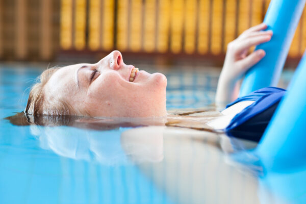 junge Frau im Pool, halb im Wasser, liegt auf einer Wassernudel im Schwimmbecken und genießt ihre Zeit im swimming pool