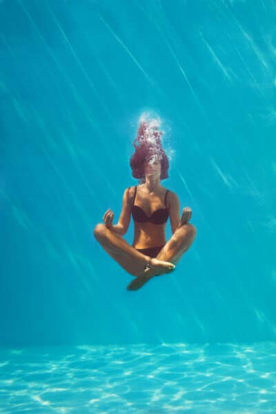eine junge Frau welche unterwasser Yoga macht young woman in black bikini in yoga position underwater in diving aquarium, full body shot, front view through the glass