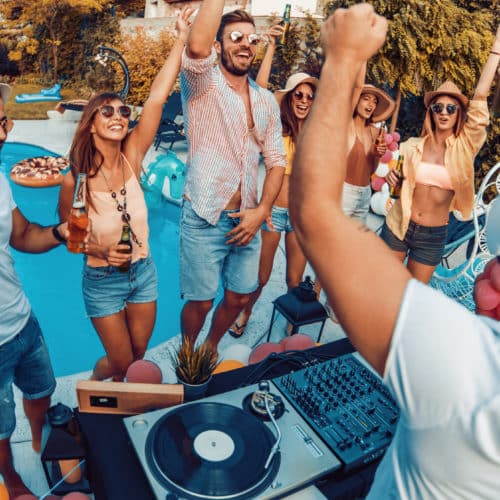 Enjoying pool party with friends.Group of friends having party by swimming pool.eine Gruppe von jungen Erwachsenen bei einer Pool Party, wie sie Musik hören, tanzen und trinken voe einem versenkten ovalen Schwimmbad