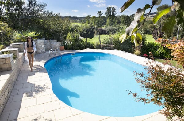 Poolgestaltung, rundherum wohlfühlen, Ovales Einbauswimmingpool, Frau am Schwimmbadrand, Steinumrandung, Pool in Gartengestaltung wunderbar eingebaut, Cranpool