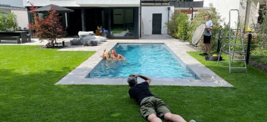Pool im Garten, Einbaubecken, steineren Schwimmbadverkleidung, Fotoshooting, zwei Personen im Pool, Fotograph liegt mit Kamera in der Wiese, Cranpool Schwimmbecken
