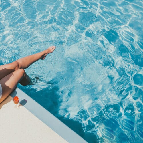Frau am Poolrand sitzend mit Füßen im Wasser