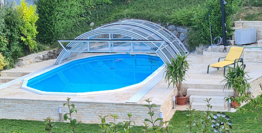 Ovales Pool mit Poolüberdachung halb offen und gepflasterter Deck 