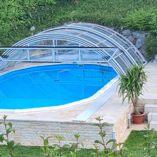 Ovales Pool mit Poolüberdachung halb offen und gepflasterter Deck