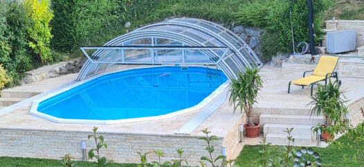 Ovales Pool mit Poolüberdachung halb offen und gepflasterter Deck