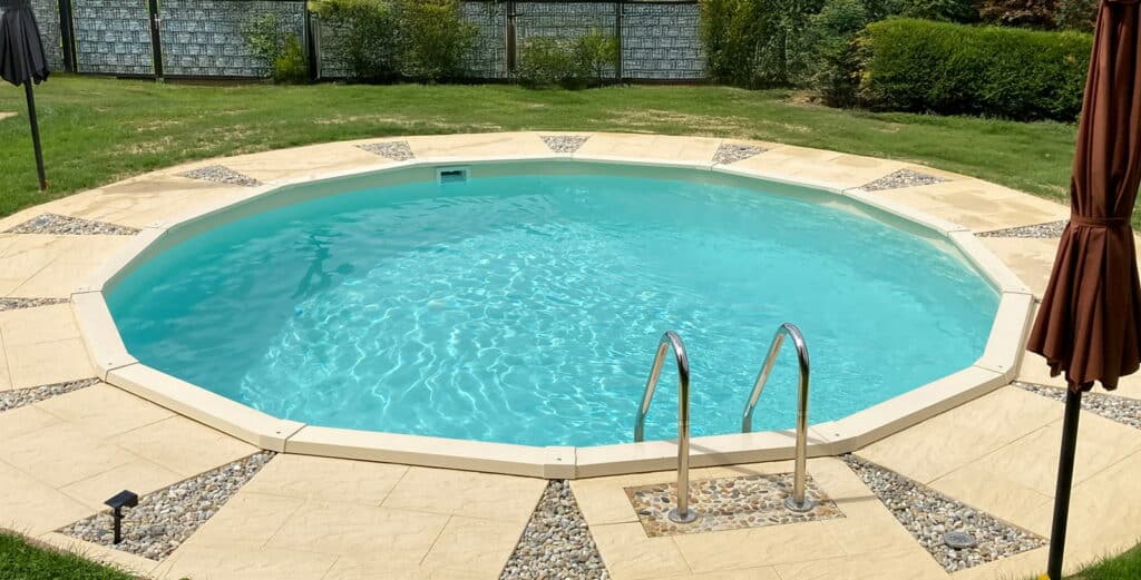 Versenkter Grand Royal Rundpool mit Einstiegstreppe und gepflasterter Poolumrandung im privaten Garten.